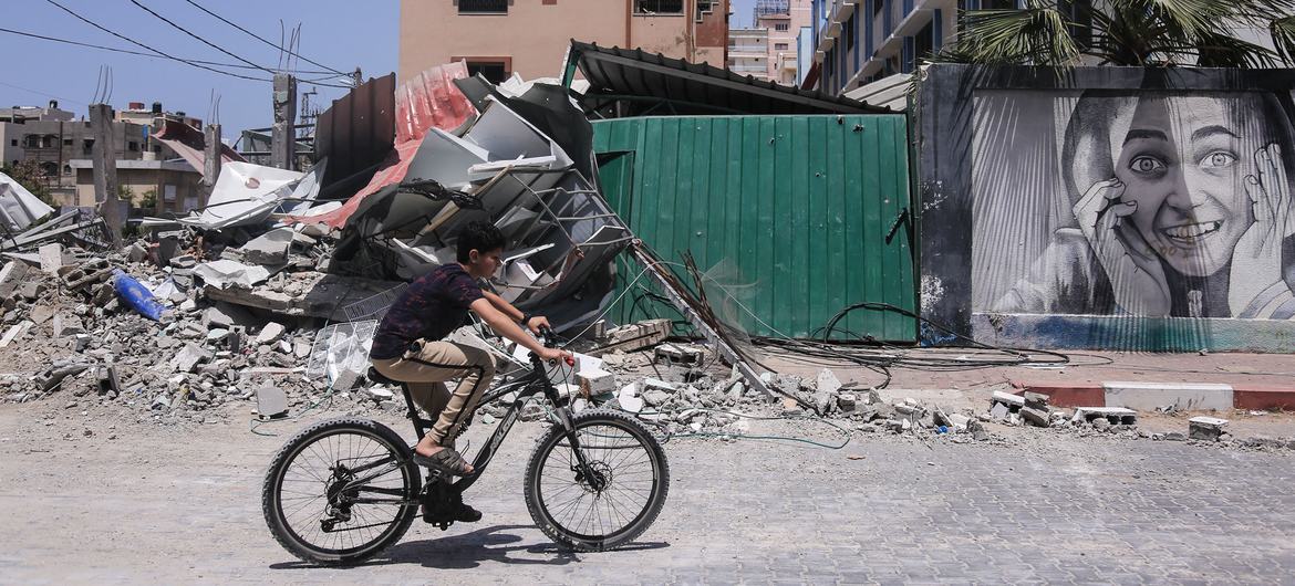 फ़लस्तीन के ग़ाज़ा पट्टी में, एक इसराइली हमले में ध्वस्त एक इमारत के पास से सायकल पर गुज़रता एक लड़का.