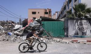 A boy rides his bike next to buildings destroyed after Israeli attacks in the Gaza Strip, Palestine.