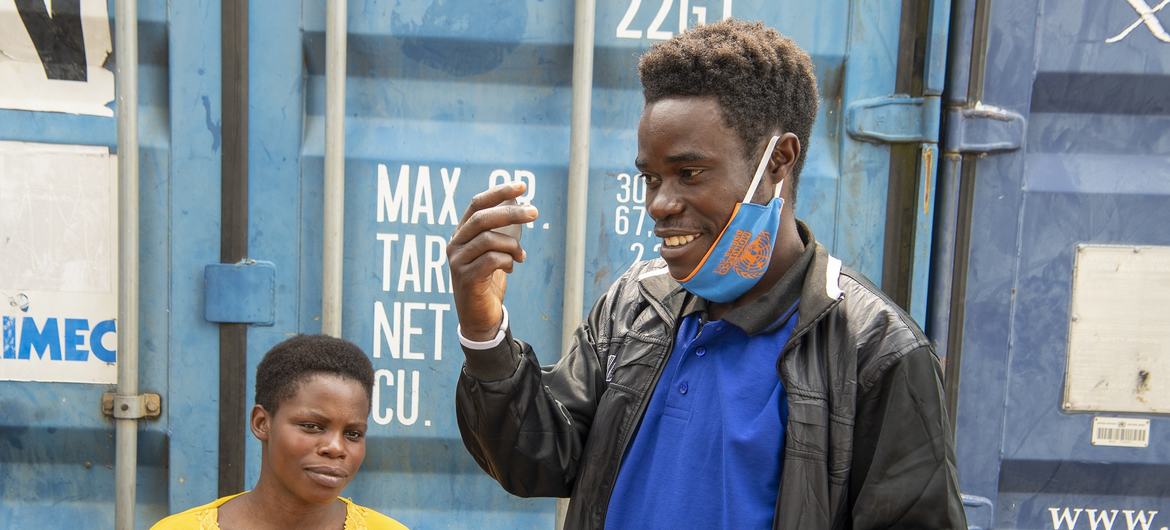 Prêt à partir ! Mukeshimana Jean-Nepo se regarde dans le miroir et sourit à sa femme qui tient leur bébé dans ses bras avant de quitter le camp de transit de Munigi à Goma, Nord-Kivu, RDC.