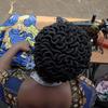 Mwanamke mwenye nywele zilizopambwa anaonekana kutoka nyuma, ameketi kwenye mashine ya kushona na akifanya kazi na kitambaa.