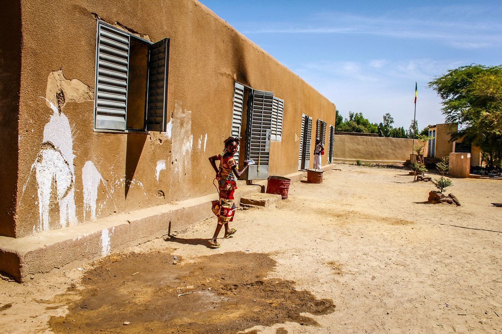 فتاة تجري خارج مدرسة صغيرة في قرية كوريوم، مالي، حيث يفتقر الأطفال إلى الأدوات الأساسية بما فيها الكتب والأقلام. جزء من المدرسة تمت مهاجمته ففي 2013 كانت القرية مقرا للمتشددين.