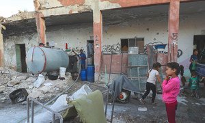 In Binnish in the Syrian Arab Republic, internally displaced people from Idlib live in a destroyed school while a tanker provides them with water that children transport with small containers.