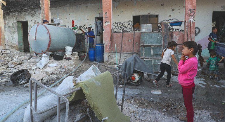 في بننيش في الجمهورية العربية السورية، يعيش النازحون داخلياً من إدلب في مدرسة مدمرة بينما تزودهم ناقلة بالمياه ومن ثم ينقلها الأطفال بحاويات صغيرة.