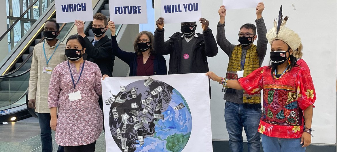 在苏格兰格拉斯哥举行的第26届气候大会上，一群手持标语的人在蓝区主走廊为摄影师拍照摆姿势。