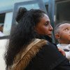 طالبة اللجوء تحمل طفلها وهي تستعد لركوب حافلة تأخذهما إلى المطار لرحلة خارج ليبيا.