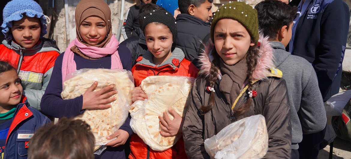 أطفال يتلقون الخبز من مخبز في حلب، سوريا، حيث يساعد برنامج الأغذية العالمي في توزيع المواد الغذائية.