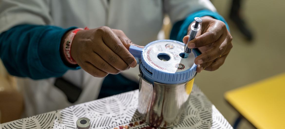 A medical worker discards a used COVID vaccine syringe into a container.