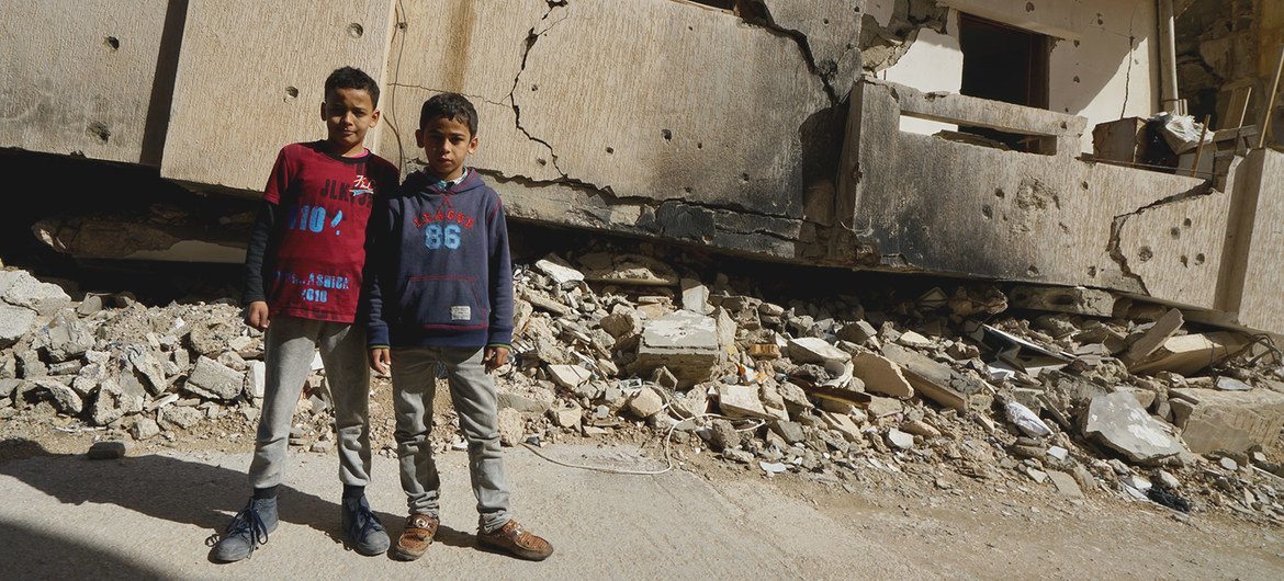 लीबिया के बेनग़ाज़ी शहर में एक ध्वस्त इमारत के पास खड़े बच्चे. 