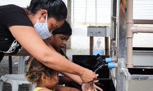 سيّدة وأطفال يستخدمون أحد مرافق غسل اليدين التي وضعتها منظمة اليونيسف في منطقة سكنية في بوا فيستا شمالي البرازيل.
