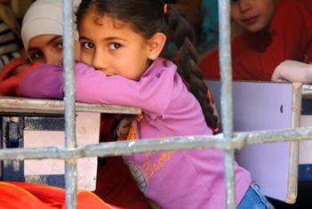 Children look through a window with bars from inside their classroom.