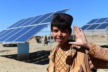 A boy waves in front of solar panels that provide electricity to pump water, in Herat, western Afghanistan. 