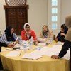 مجموعة من النساء المحجبات يجلسن حول طاولة مستديرة خلال اجتماع، وأمامهن أوراق وزجاجات مياه.
