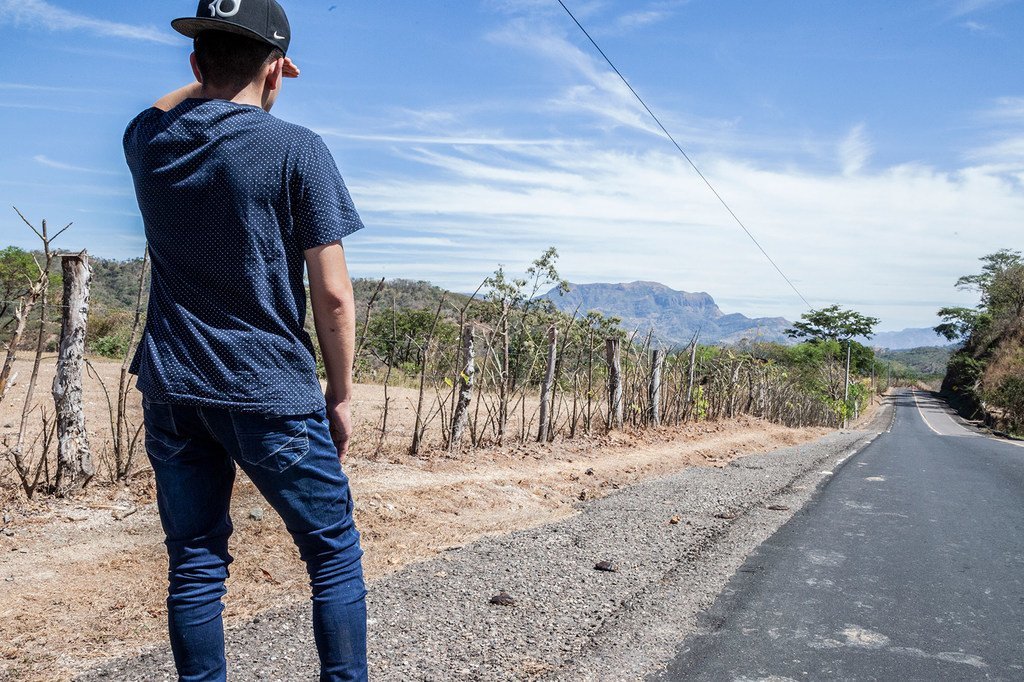 Un jeune homme déplacé se tient au bord d'une route d'El Salvador.