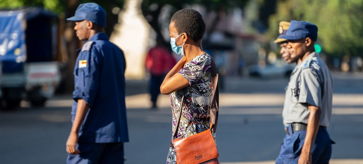 A woman wearing a COVID-19 protective mask walks past a group of police officers on patrol in Harare, Zimbabwe.