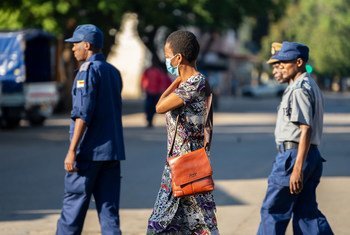 A woman wearing a COVID-19 protective mask walks past a group of police officers on patrol in Harare, Zimbabwe.
