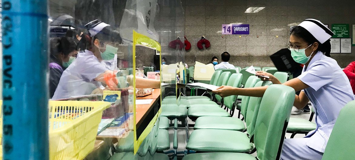 Nurses at a hospital in Bangkok, Thailand, exchange documents through acrylic shields that have been setup to ensure physical distancing. 