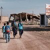 أطفال يسيرون إلى جانب لافتة تحذر المجتمعات المحلية من وجود الألغام، بما في ذلك الألغام بدائية الصنع، في تلعفر بالعراق.
