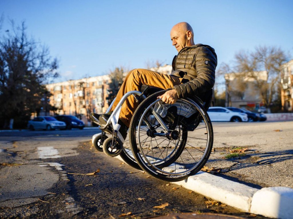 Foto de un hombre en sillas de rueda intentando superar un bordillo en la calle