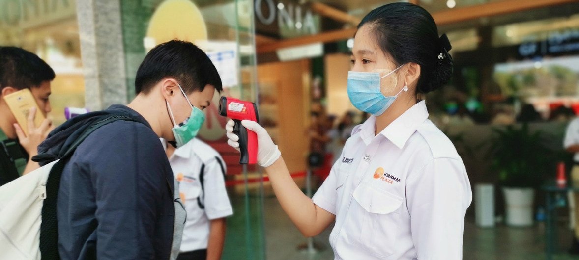 Trabajadores toman la temperatura de los clientes para descartar el coronavirus en un centro comercial de Yangon, Myanmar.