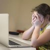 Una joven sentada frente a una computadora portátil tapándose la cara con las manos en Podgorica, Montenegro.