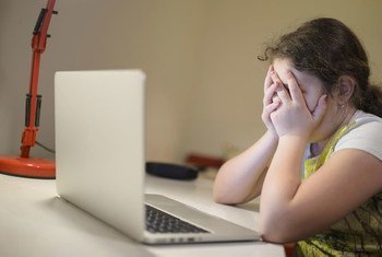 Young girl in Podgorica, Montenegro, sits in front of a laptop holding her head in her hands.