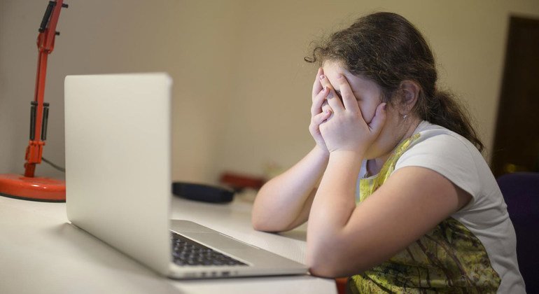 A young girl in Podgorica, Montenegro, sits in front of a laptop holding her head in her hands.