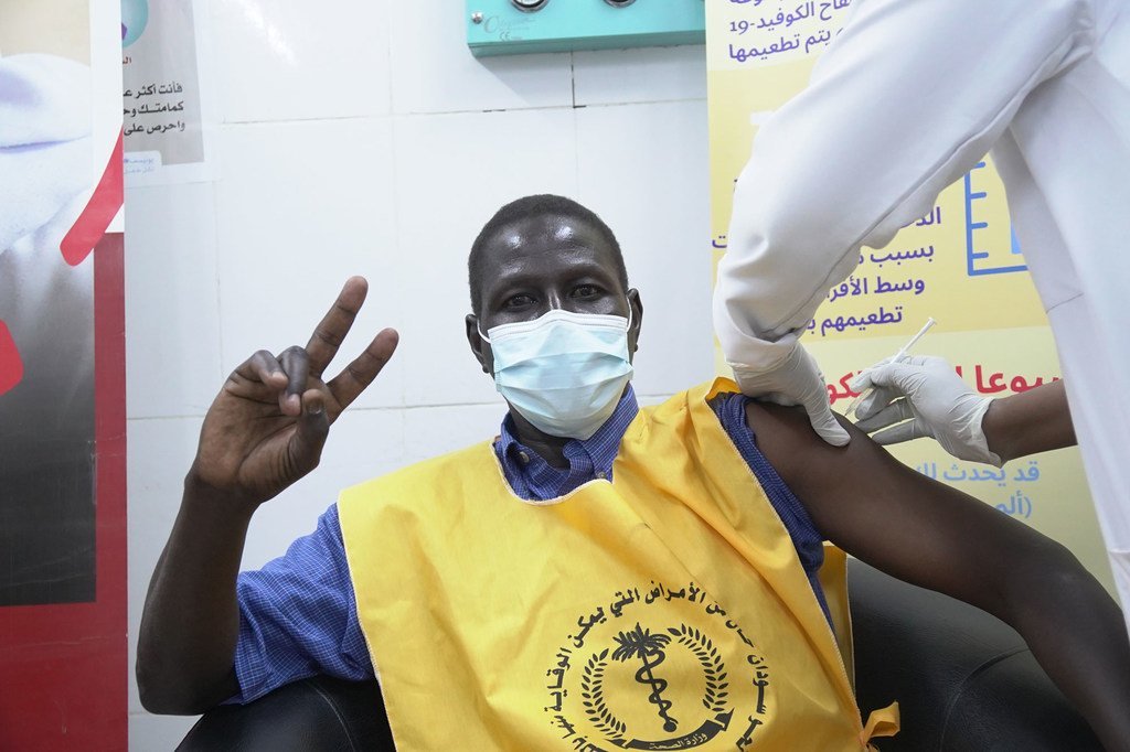 أحد العاملين في مجال الرعاية الصحية في السودان يرفع علامة النصر أثناء تلقيه لقاح كوفيد-19. 