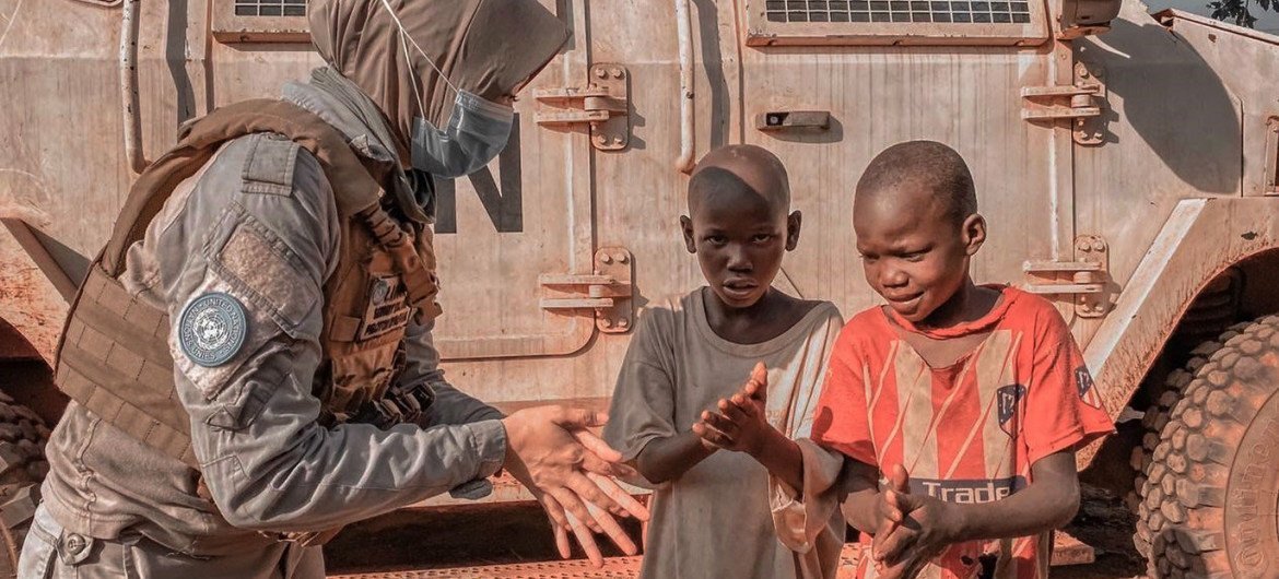 A peacekeeper with MINUSCA, the UN mission in the Central African Republic, explains to two young boys how to properly apply hand sanitizer as protection against coronavirus.
