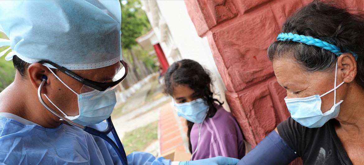 El Dr. Douglas Martínez toma la presión arterial de un migrante venezolano que regresa a la cuarentena en un refugio temporal durante Covid-19.