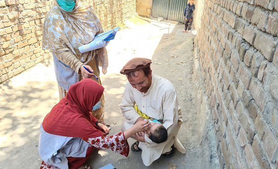 No Afeganistão, pai segura filho enquanto funcionários de saúde o vacinam