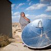 अफ़ग़ानिस्तान में सौर ऊर्जा से खाना पकाने में मदद करने वाली डिस्क के पास खड़ी एक महिला.