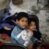 加沙城内的一个贫民区，10岁的伊布拉辛（左）抱着一直猫坐在自家简易的房屋门前。
