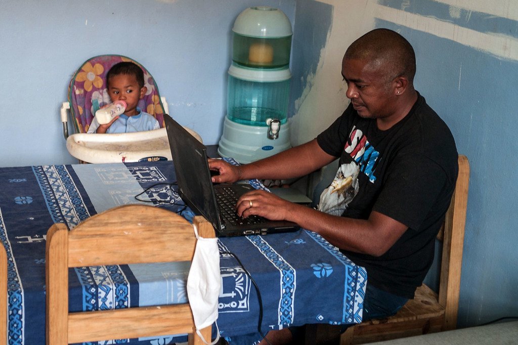 Un père s'occupe de son jeune enfant tout en travaillant à la maison à Madagascar.