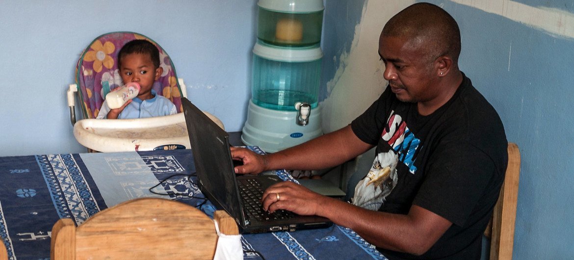 Un père s'occupe de son jeune enfant tout en travaillant à la maison à Madagascar.