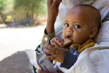 A seven-month-old baby displaced with his mother due to conflict in Tigray eats a high energy biscuit to boost his nutrition levels.