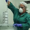 Una científica, vestida con un traje protector verde, respirador y gafas de seguridad, trabaja en un laboratorio con un contenedor criogénico.