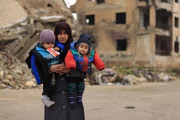 سيّدة تحمل طفليْها في مدينة حلب التي تعرّضت للدمار في سوريا