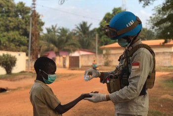 Un miembro del personal de mantenimiento de la paz de la Misión de Estabilización Integrada Multidimensional de las Naciones Unidas en la República Centroafricana (MINUSCA) vierte gel desinfectante en la mano de un niño.