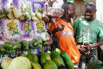 Des marchands ambulants discutent devant leur étal de fruits et legumes sur un marché de Kampala, en Ouganda