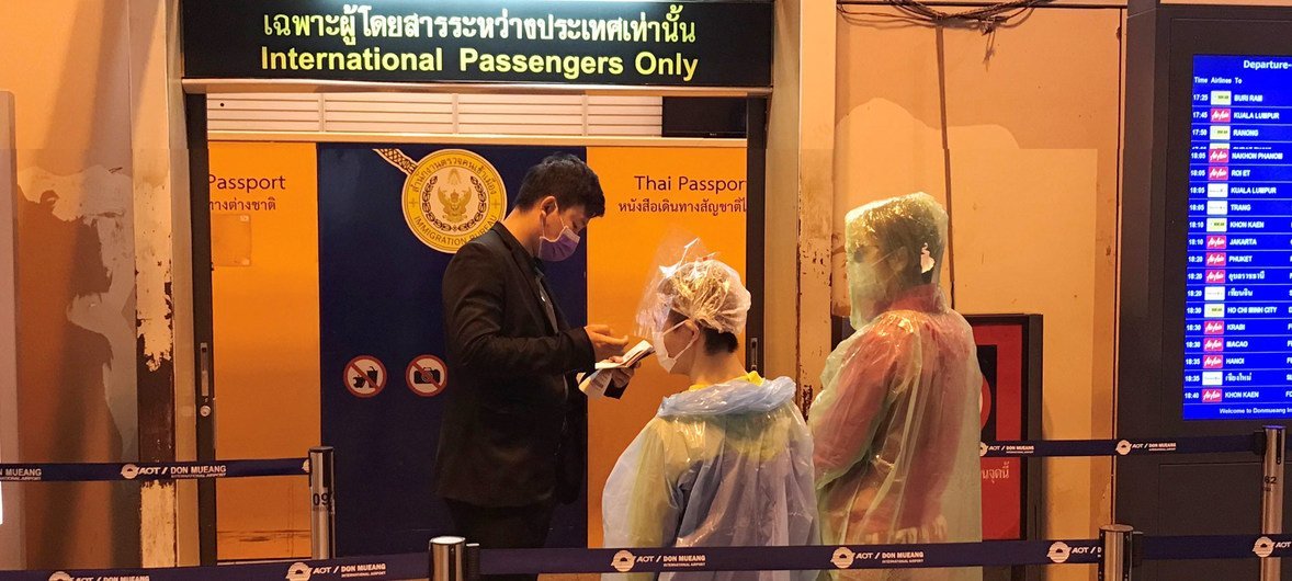 Des passagers portant des masques faciaux et des ponchos jetables font vérifier leur passeport à l'aéroport international Don Mueang de Bangkok, en Thaïlande.