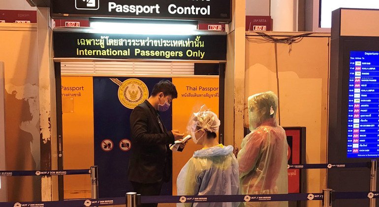 मास्क सहित बचाव पोशाक पहने यात्री थाईलैंड के बैंकॉक एयरपोर्ट पर अपने पासपोर्ट की जांच करवाते हुए. 