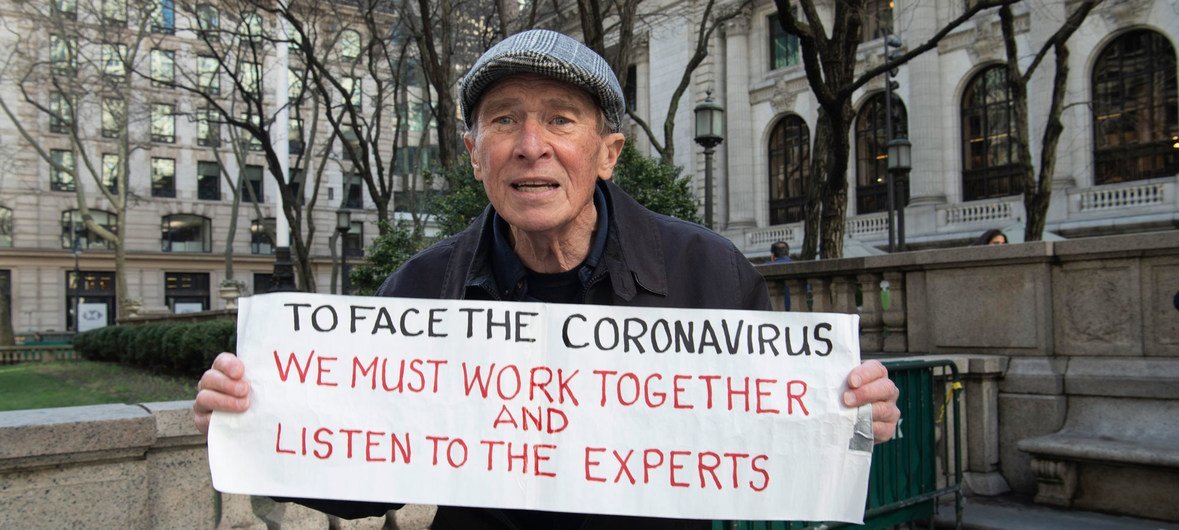 Un ciudadano de Nueva York con una pancarta en la que se lee: Para afrontar el coronavirus, debemos trabajar juntos y escuchar a los expertos.