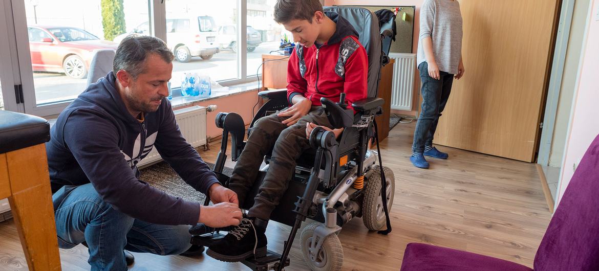Un padre ayuda a su hijo con parálisis cerebral a acomodarse en su silla de ruedas eléctrica.