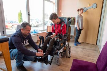 在科索沃，一位父亲帮助患有脑瘫的儿子坐到电动轮椅上。