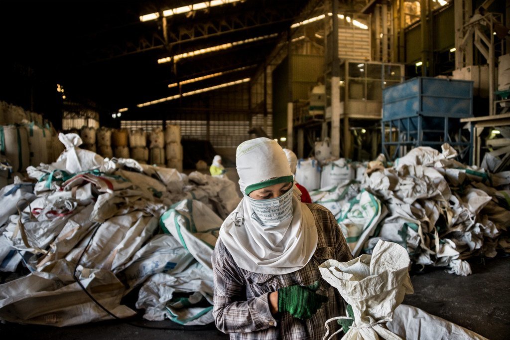 一名缅甸的移民劳工正在泰国乌汶府的一家碾米厂工作。每天都有几百个用过的米袋被送回到厂里，经过分拣、清洗和修补后再投入二次使用。