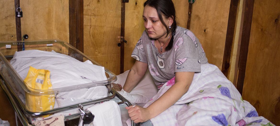 A new mother sits in a bed next to her baby in a makeshift maternity ward in a hospital in Kyiv, Ukraine.