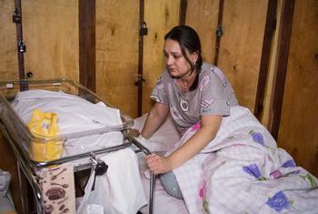 A new mother sits in a bed next to her baby in a makeshift maternity ward in a hospital in Kyiv, Ukraine.