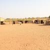 Une école au Niger, avec un bâtiment moderne et plusieurs huttes traditionnelles en paille, dans un paysage aride et sablonneux.