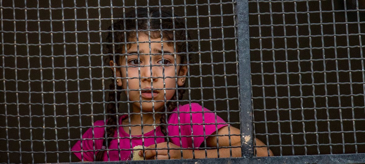 On 11 October 2019 in the Syrian Arab Republic, a girl stares out from behind a metal grilled window where families displaced from Ras al-Ain have arrived in Tal Tamer, having fled escalating violence.