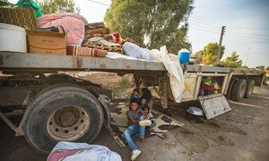 On 11 October 2019 in the Syrian Arab Republic, a woman and children sit underneath a truck as people displaced from Ras al-Ain arrive in Tal Tamer, having fled escalating violence.